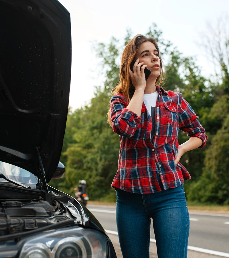 Una chica de pie al lado del coche gestionando siniestro por teléfono.